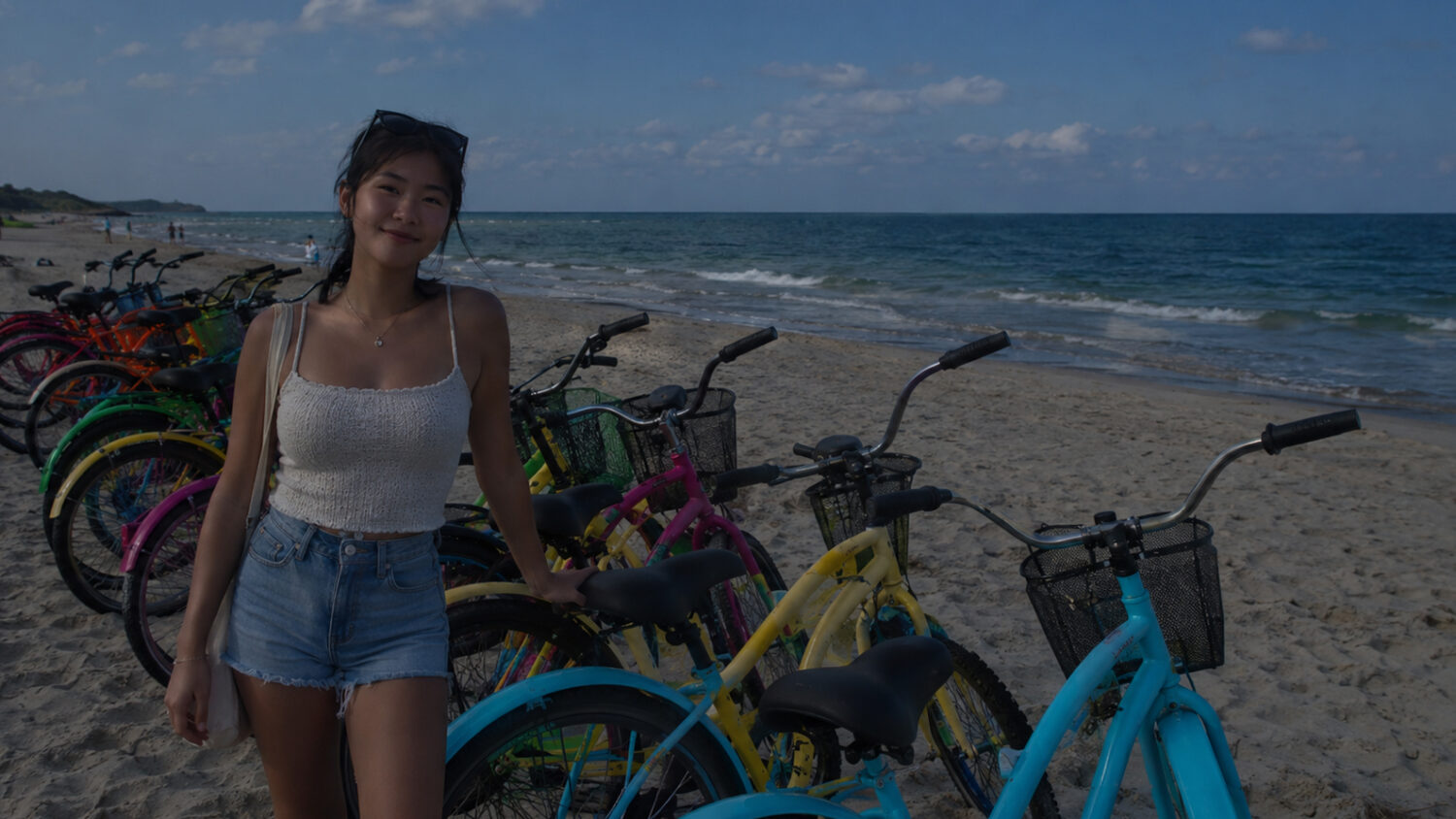 Poorly lit photo taken of a woman standing by bikes on the beach shore.